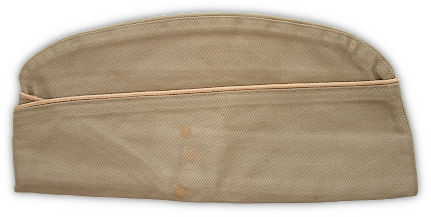 Left side view of the khaki cotton field cap. The cap had a bellows crown and a turned‐up curtain that crossed in the front. Authorization was given for the cap to be trimmed in branch of service colored cord‐edge braid.  The piping was worn in much the same manner that branch of service cords were worn around the crown of the olive‐drab service hat. In this case the buff‐colored trim indicates the Quartermaster Corps.