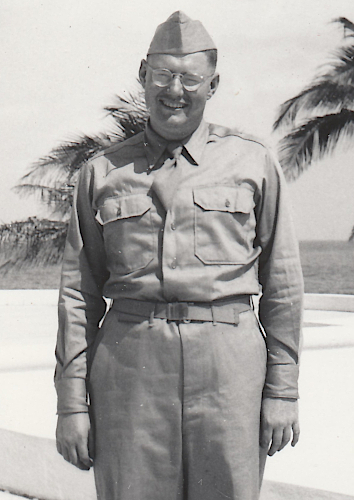 Army Air Force Pvt. Elmer Goll in Miami Florida in February 1943. Pvt. Goll wears the convertible collar khaki cotton shirt approved in 1941.  This shirt was designed to maintain an acceptable military appearance with its collar open without a necktie or closed with a necktie.  The sports collar made wear in the field more comfortable where a necktie was not required.  Identification of this shirt is made easy by its lack of a front button placket.   Note the dished zinc waistband button visible just underneath the nonregulation solid belt buckle. Dished buttons were a feature of early production specification 6‐254 khaki trousers.