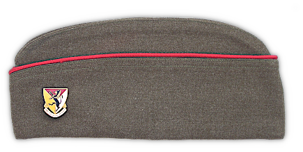 Left side view of the olive drab field cap. Army regulations allowed for colored branch of service corded braid to be worn on the edge of the cap. In this case, the scarlet color represents both the field artillery and costal artillery branches. Additionally, regulations allowed for the wearing of distinguished unit insignia at the front of the cap on the left side. Attached is the crest representing the 124th Field Artillery Regiment attached to the 33rd Infantry Division.