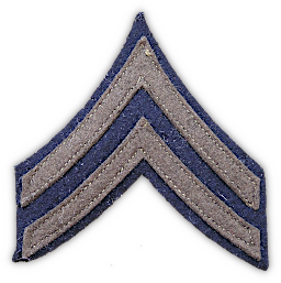 Close‐up view of wool corporal chevrons (fifth grade). Noncommissioned officers and first class privates wore insignia of grade on the wool uniform that included olive‐drab wool chevrons, arcs, and a lozenge on a dark blue wool background. The background was to form an edging around the entire insignia and between the chevrons. Chevrons were worn on the wool coat, overcoat, and shirt and were located on the outside of the sleeve approximately halfway between the shoulder and elbow. Separate, washable cotton chevrons were made for wear on the cotton shirt.