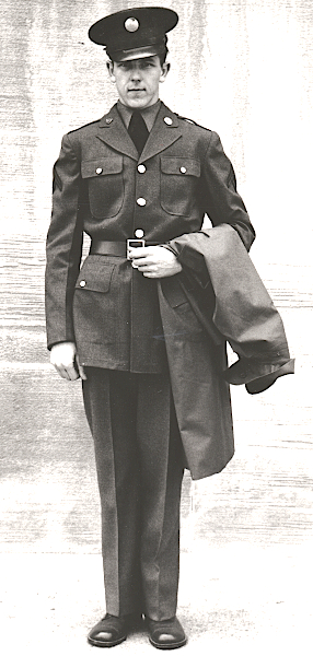 U.S. Army photograph taken on 20 June 1941 showing the enlisted man's wool dismounted uniform for garrison. The soldier wears the olive‐drab service cap, flannel shirt, black necktie, 18‐ounce serge wool coat with leather belt, 18‐ounce serge wool trousers in "light shade", and russet colored service shoes. Draped over his left arm is the M‐1938 raincoat.