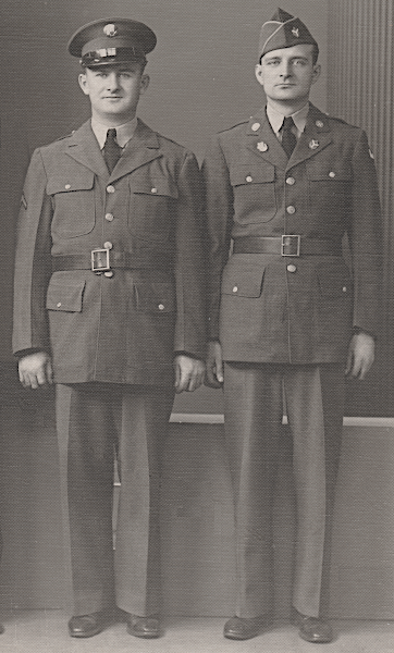 Two GIs wear the wool garrison uniform. To accentuate his uniform, the soldier on the left wears a service cap and leather belt that are both private purchase. The soldier on the right wears the olive‐drab field cap with branch of service trim and distinctive unit insignia on the left side. He also wears the distinctive insignia on the lapels of his coat. Both soldiers are wearing the khaki cotton shirt with black necktie.