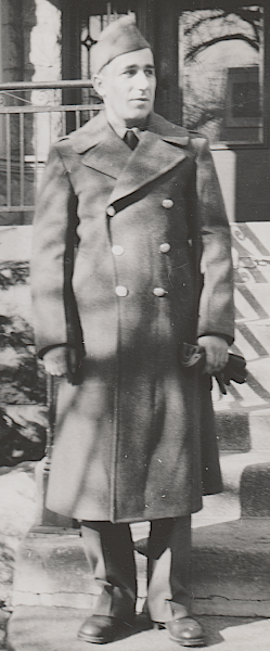Soldier wearing the olive‐drab wool service uniform with overcoat. The 32‐ounce olive‐drab melton wool overcoat was worn over the wool garrison uniform when conditions warranted it. This overcoat was standard issue in regions with a winter season. In the soldier's left hand are a pair of olive‐drab woolen gloves.